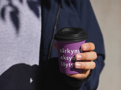 Kädessä kertakäyttö kahvimuki, jossa teksti "särkynyt, eksynyt, löytynyt".