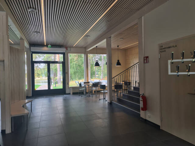 Avara ja moderni sisääntuloaula, jossa on oleskelutilaa, portaat ylempiin majoitustilaan ja näkymä vehreään pihapiiriin.