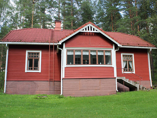 Perinteinen punainen torpparakennus luonnon keskellä, vaalea ikkunakehys ja vehreä piha-alue.
