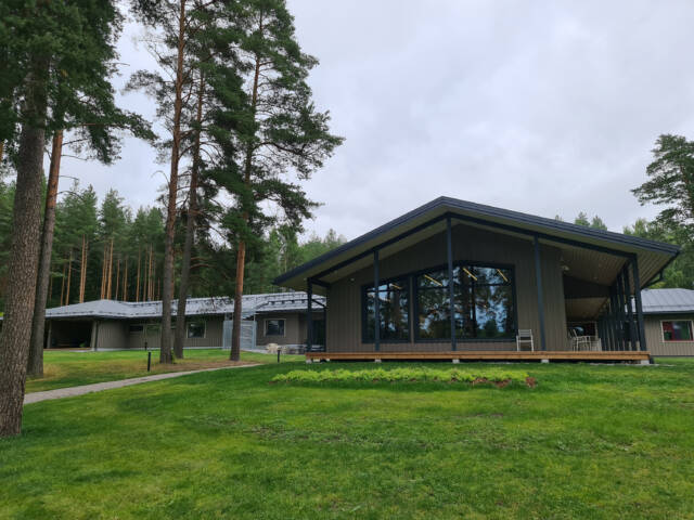 Puinen leirikeskusrakennus nurmikentän keskellä, suuret ikkunat avautuvat järven suuntaan.