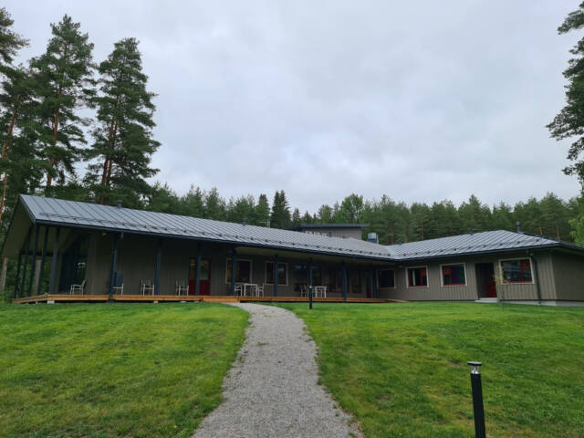 Laaja rakennus piha-alueen keskellä, katettu terassi ja kävelypolku kutsuvat sisään.